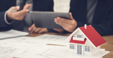 Image of two people looking at a tablet with a miniature of a house in the foreground